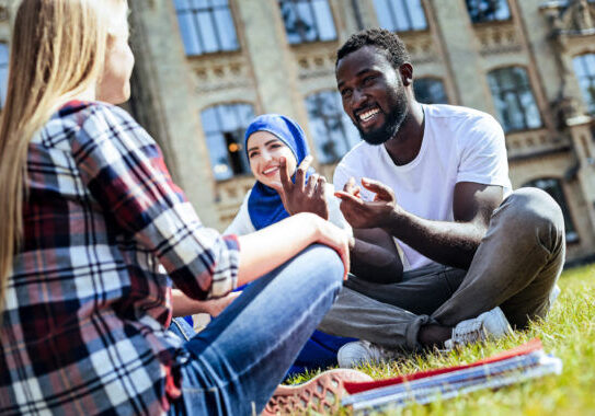 Pleasant conversation. Low angle shot of young people grinning broadly while sitting on grass and chatting together outdoors.