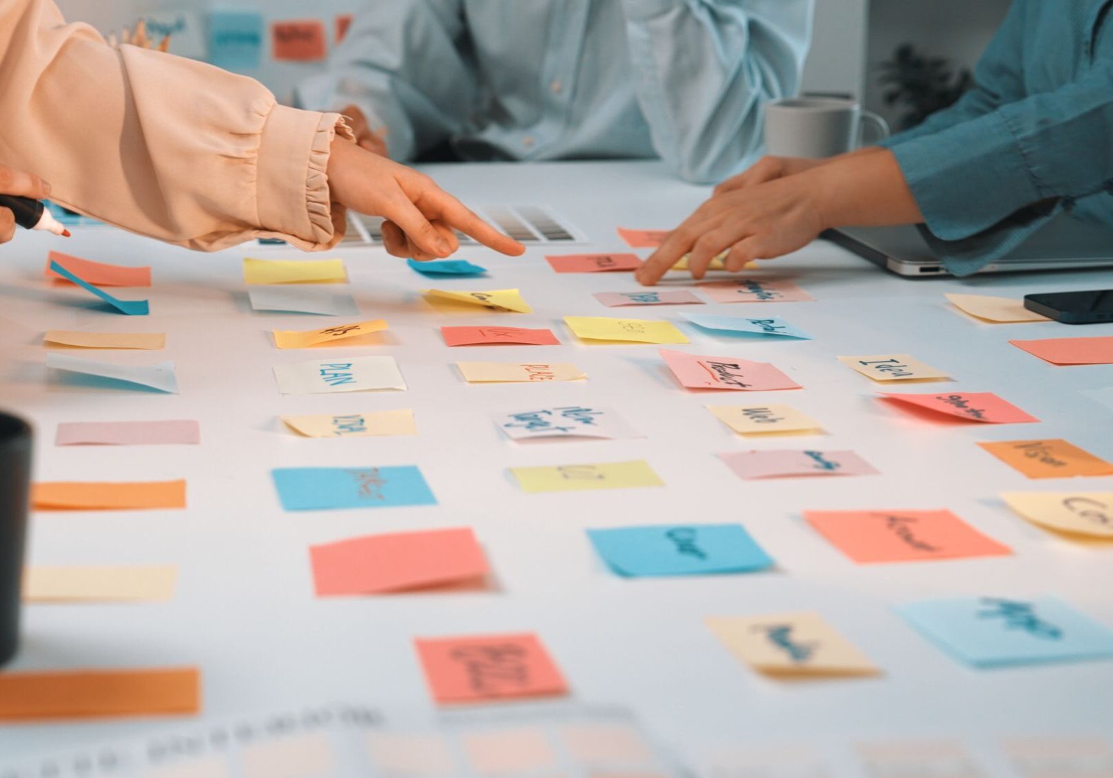 A vibrant scene of diverse hands reaching for colorful sticky notes on a white table, highlighting creative collaboration and brainstorming in a modern workspace setting. SACTR